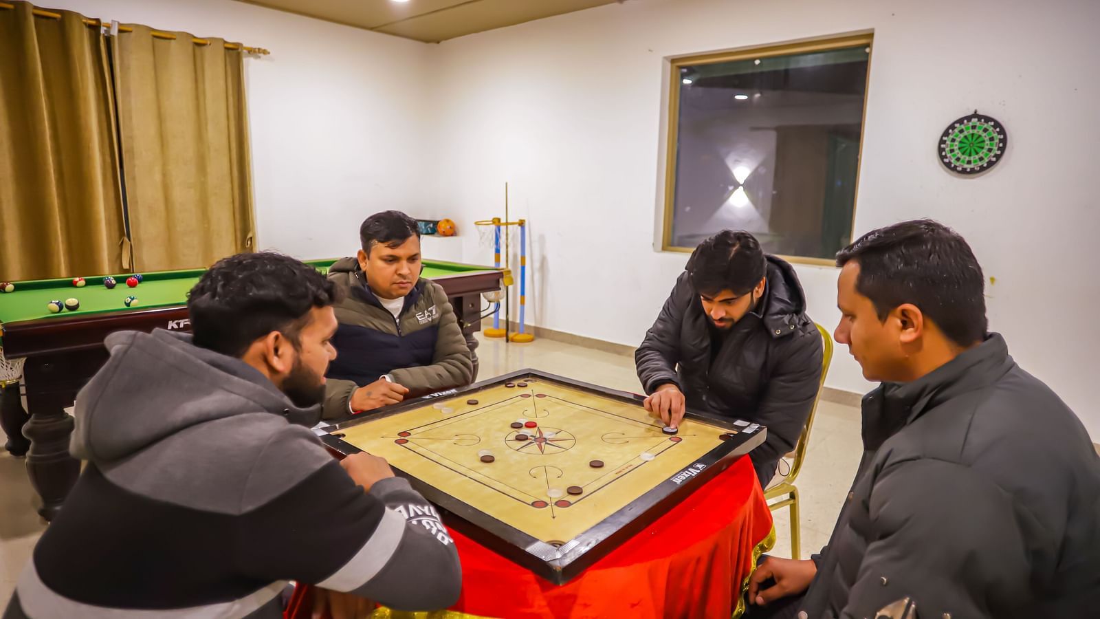 Guests play a board game at a table in a well-lit room at Vedikant Resorts The Mallard Corbett.