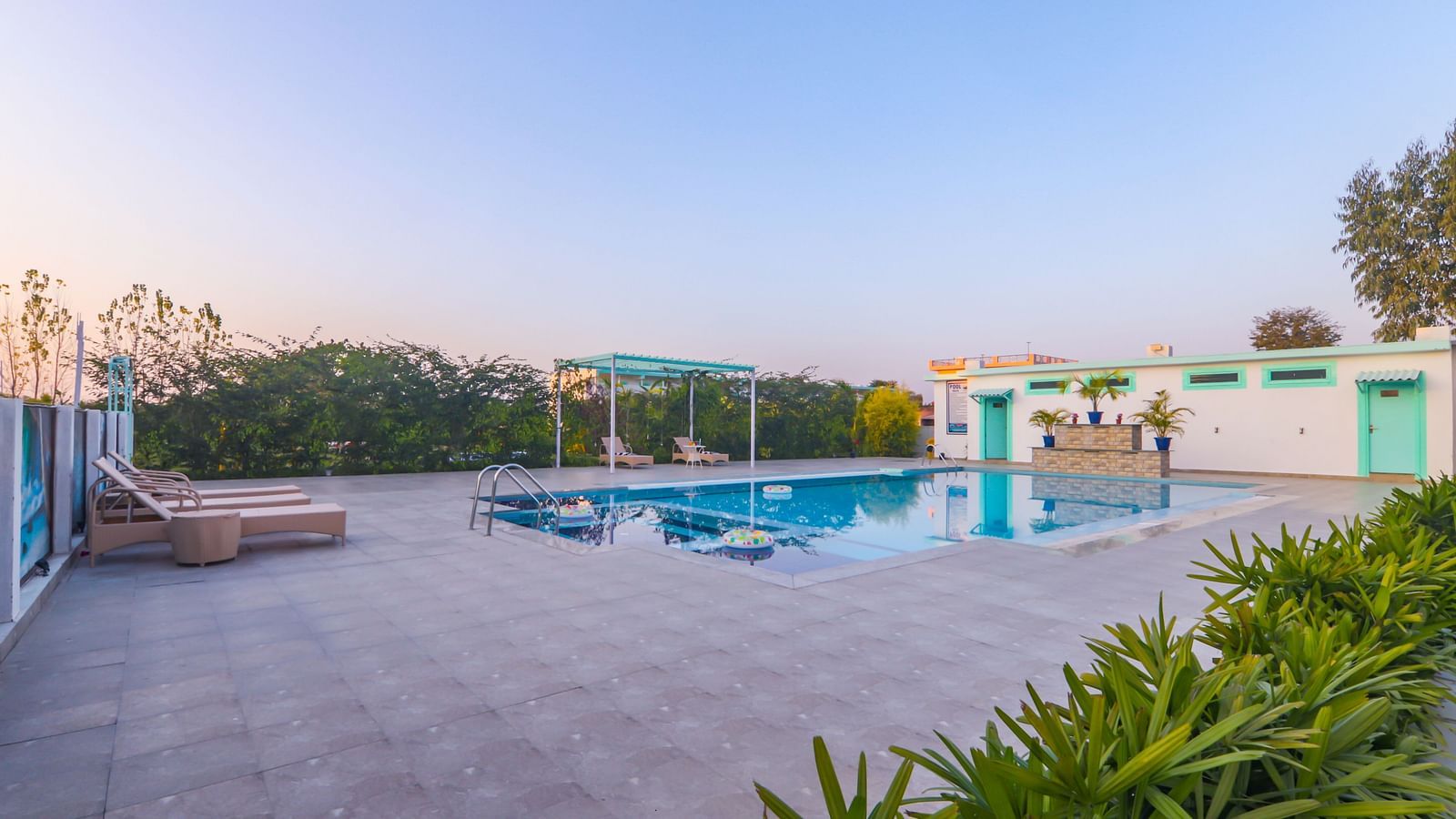 View of a swimming pool with buildings, trees and clear blue sky in the background - Vedikant Resorts The Mallard Corbett.