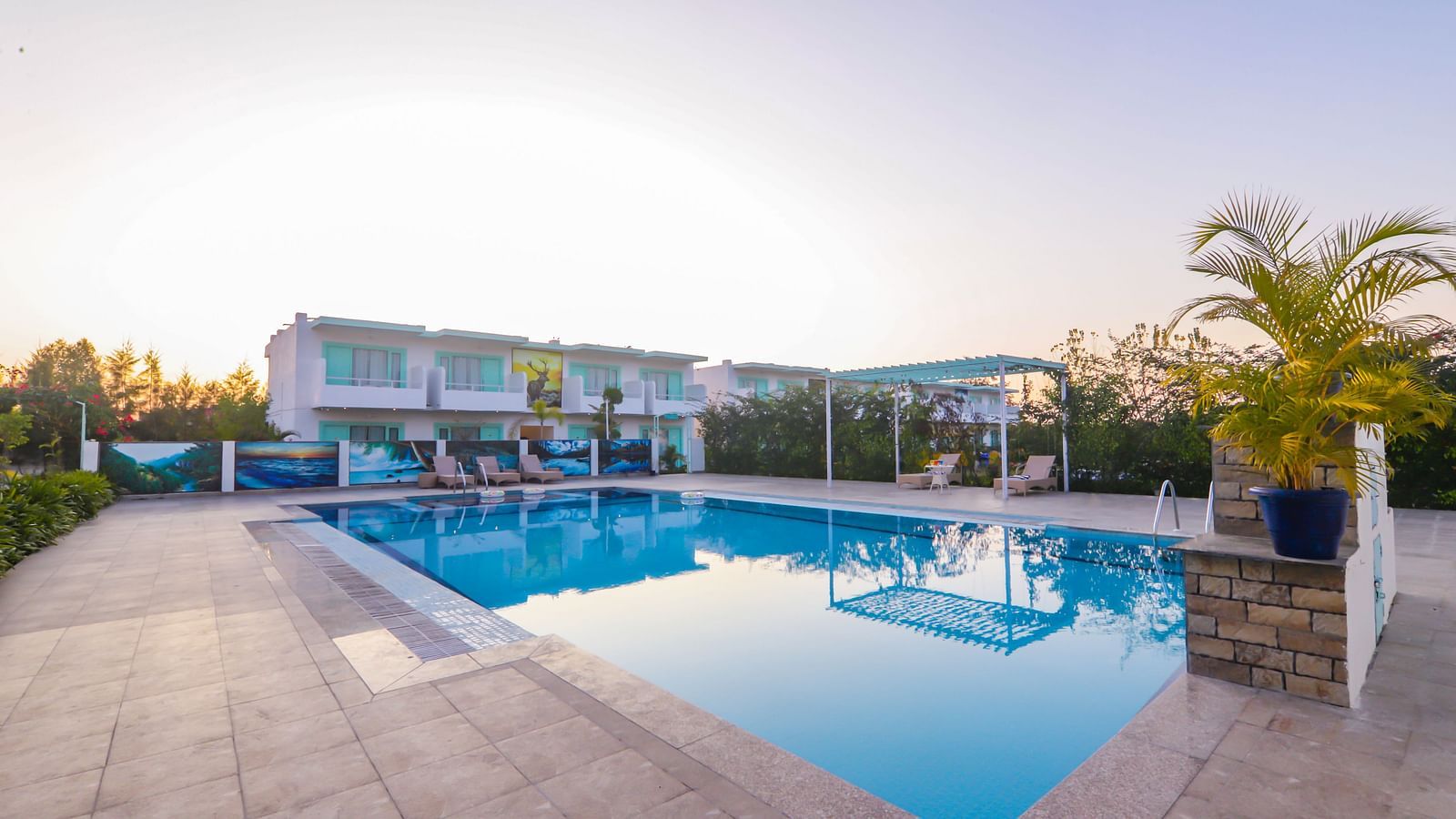 View of a swimming pool with buildings, trees and clear blue sky in the background - Vedikant Resorts The Mallard Corbett.