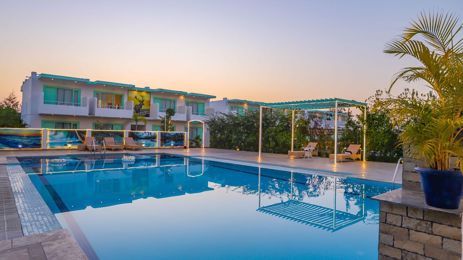 View of a swimming pool with trees, buildings and clear blue sky in the background - Vedikant Resorts The Mallard Corbett.
