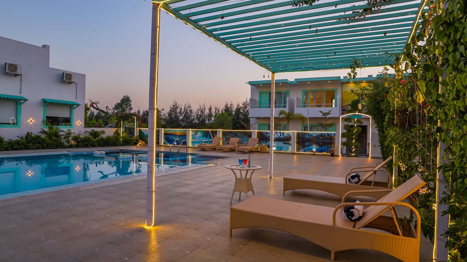 View of a swimming pool with sun lounger, trees, buildings and clear blue sky in the background - Vedikant Resorts The Mallard Corbett.