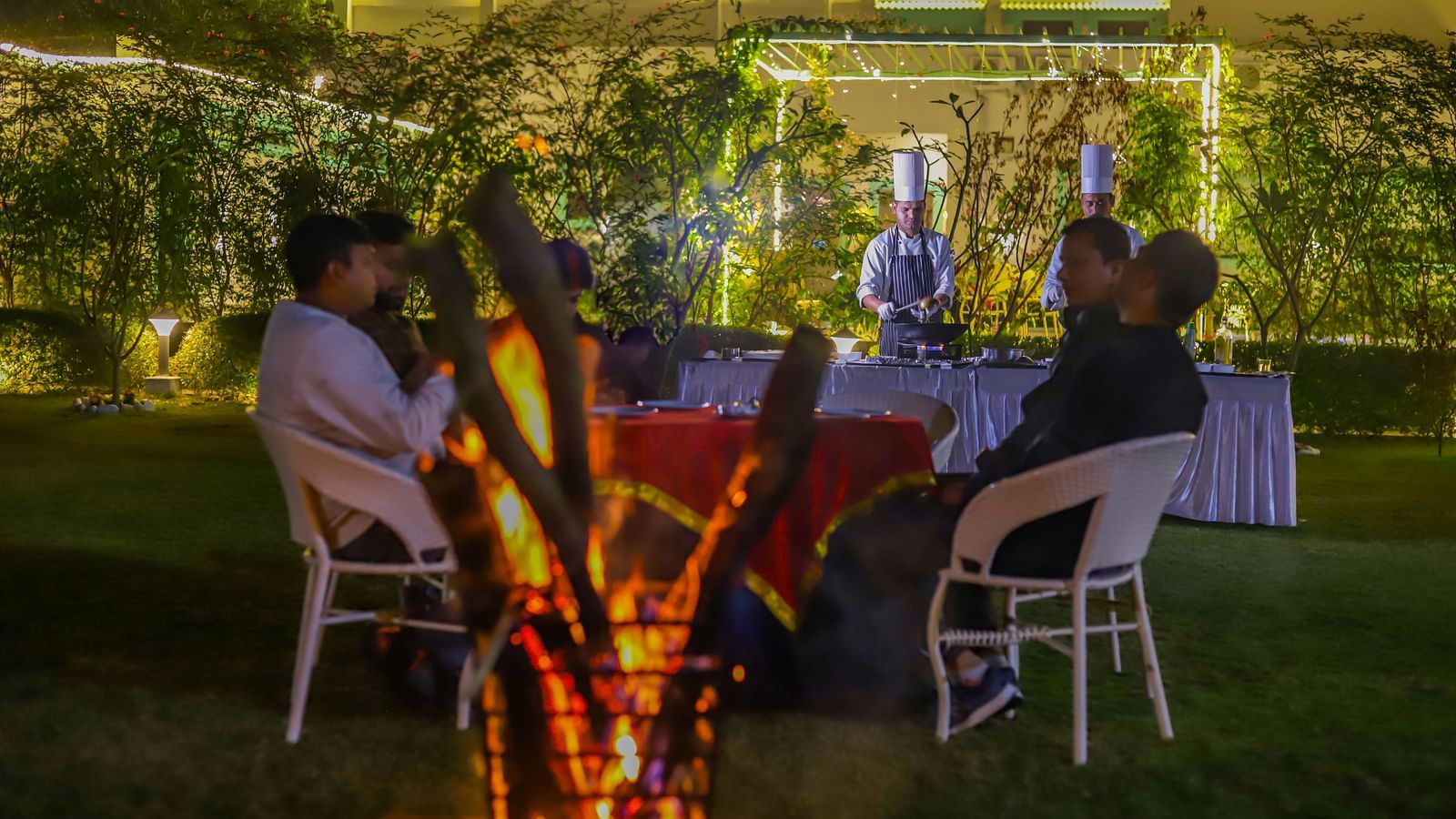 Guests dine outdoors at Vedikant Resorts The Mallard Corbett with tables and chairs arranged on a lawn under decorative lighting.