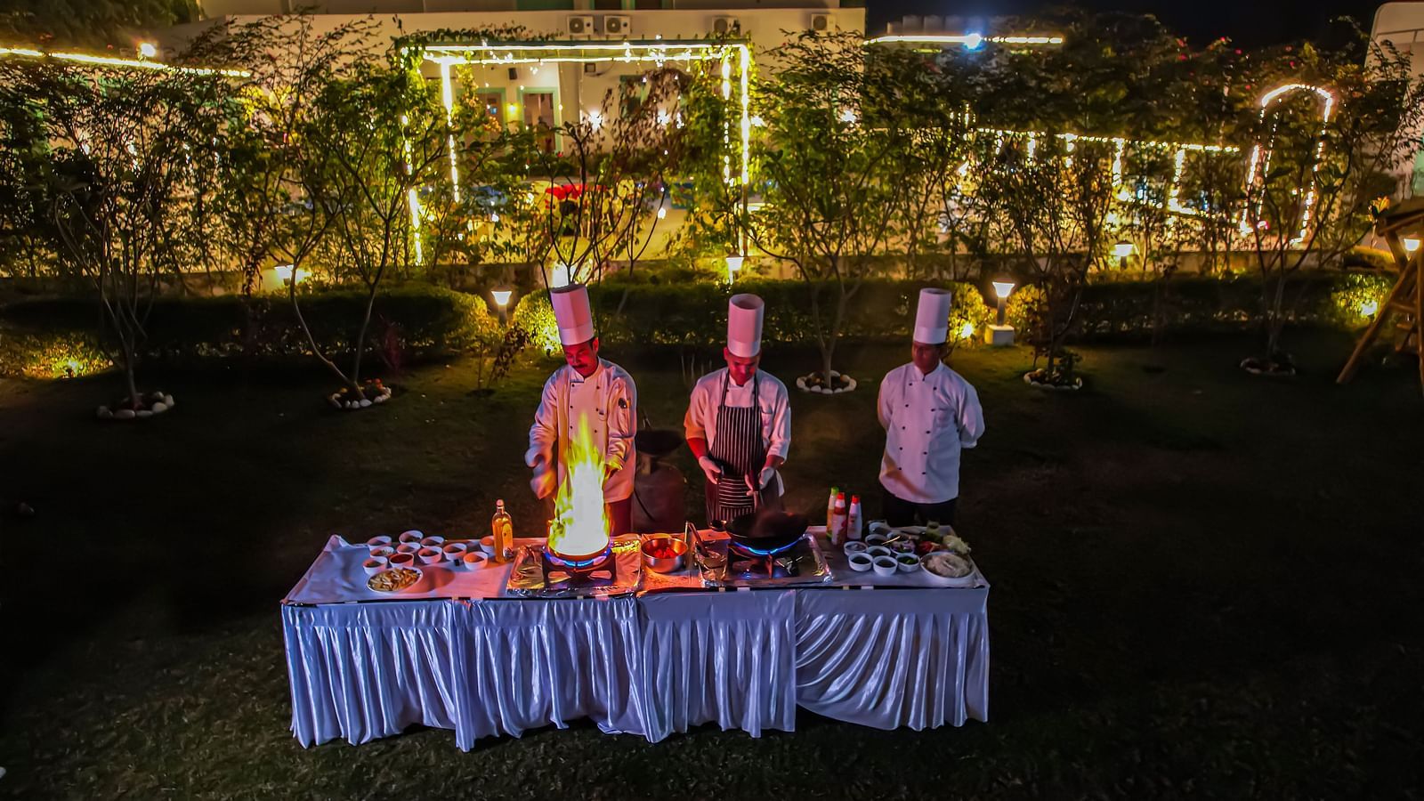 Chefs stand behind a decorated food display at night at Vedikant Resorts The Mallard Corbett, with buildings and lights in the background.