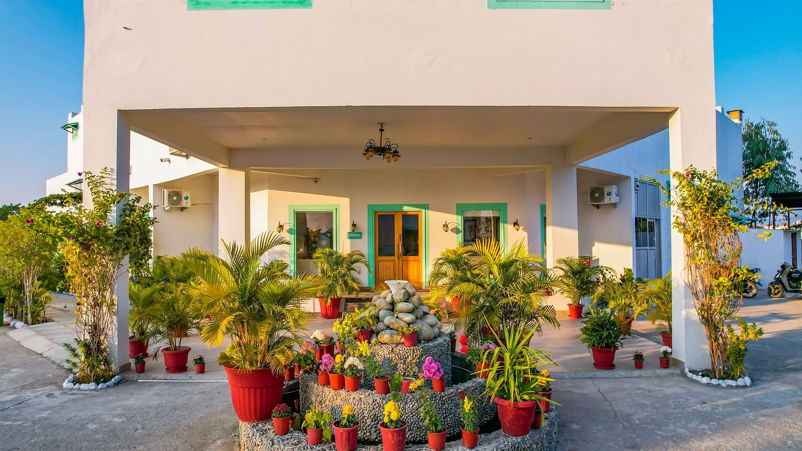 Front entrance of Vedikant Resorts The Mallard Corbett with flowerpots, plants, and covered veranda supported by pillars.