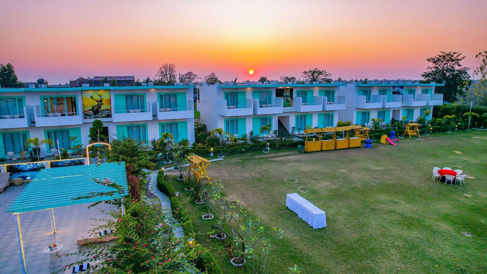 Lawn with outdoor dining tables at Vedikant Resorts The Mallard Corbett facing rows of rooms under a setting sun.
