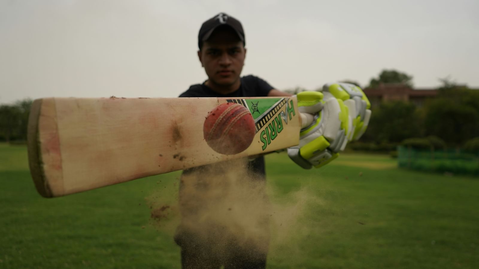 A boy playing cricket outdoors swinging a bat at the ball.