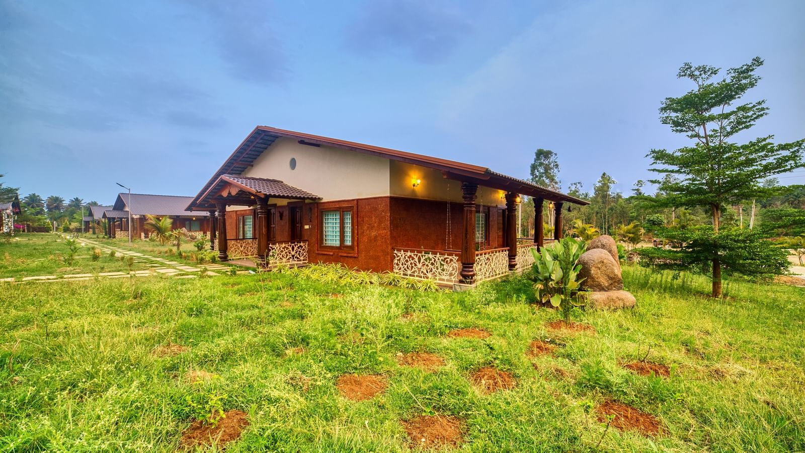 A single-storey cottage-style building with a sloping roof and a porch, set in an open grassy field with distant trees under a clear sky. - Vintage Trails by Ilara