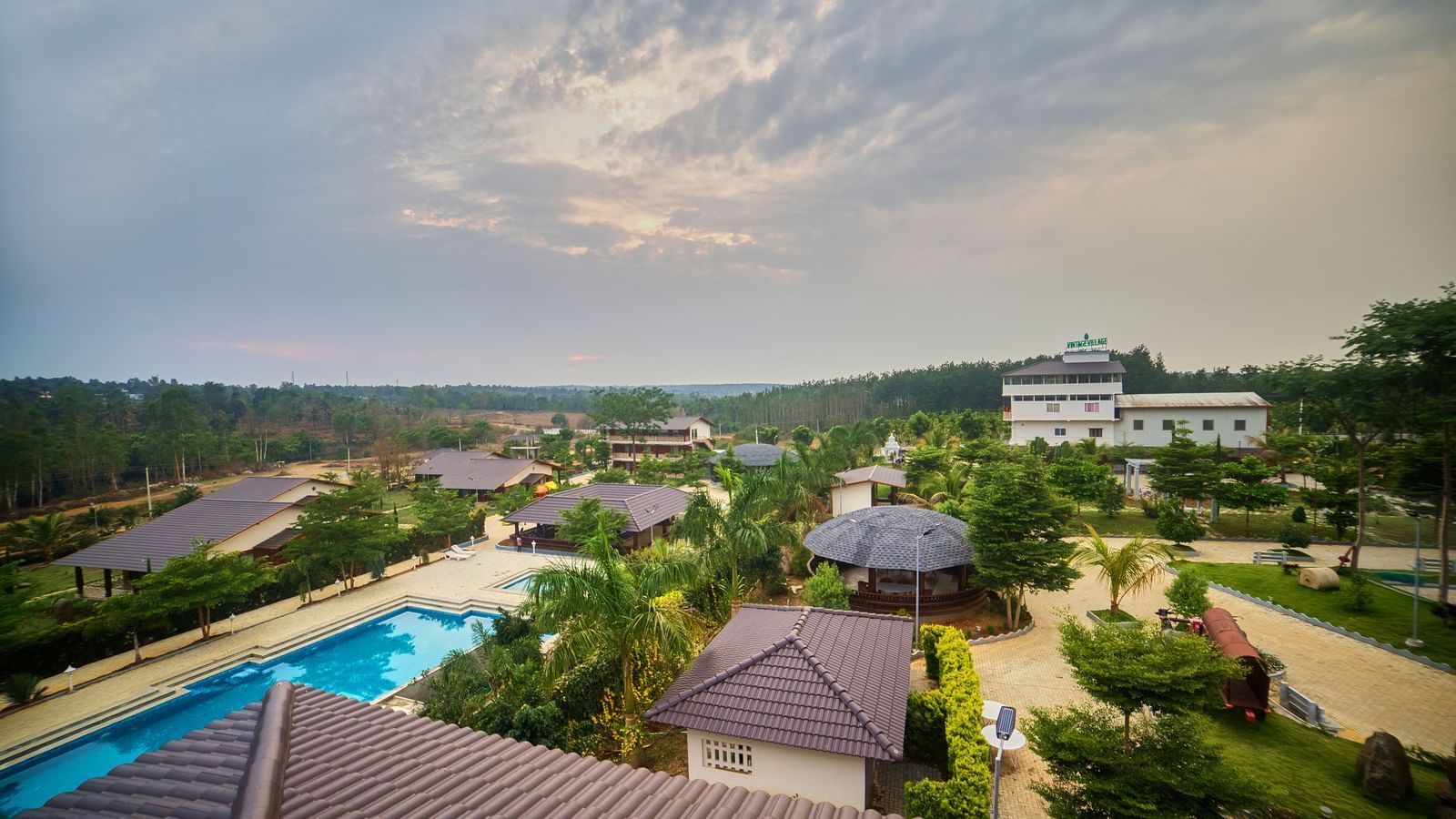 An elevated view of a resort complex featuring buildings with brown roofs, several swimming pools with blue water, and winding pathways, all set within a vast landscape - Vintage Trails by Ilara