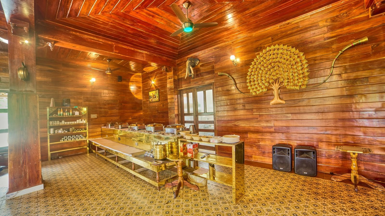 A warmly lit room with rich wooden panelled walls and ceiling, featuring decorative lighting, colourful accents, and an open seating area, possibly a dining or common space. - Vintage Trails by Ilara