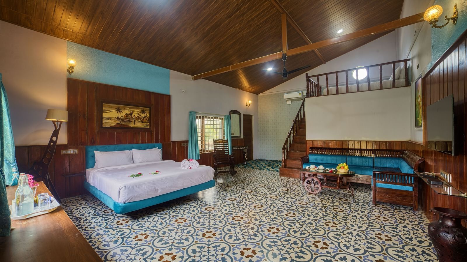 The interior of a bedroom or common area with a patterned tiled floor, a large bed with a light blue bedspread, and ceiling, and a seating area with a sofa. - Vintage Trails by Ilara