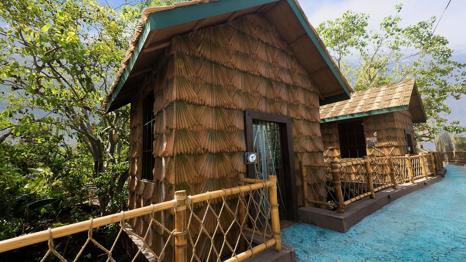 Rustic wooden cabin with a balcony and railing, surrounded by trees and greenery on a path.