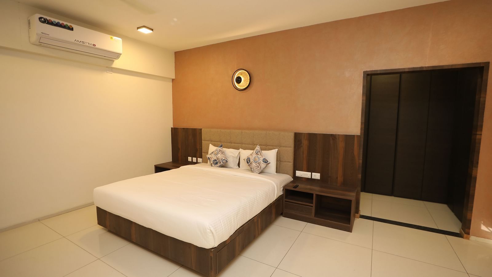 A bedroom with a large bed on a wooden frame, wall-mounted AC and a night stand - Welcome Inn Hotels