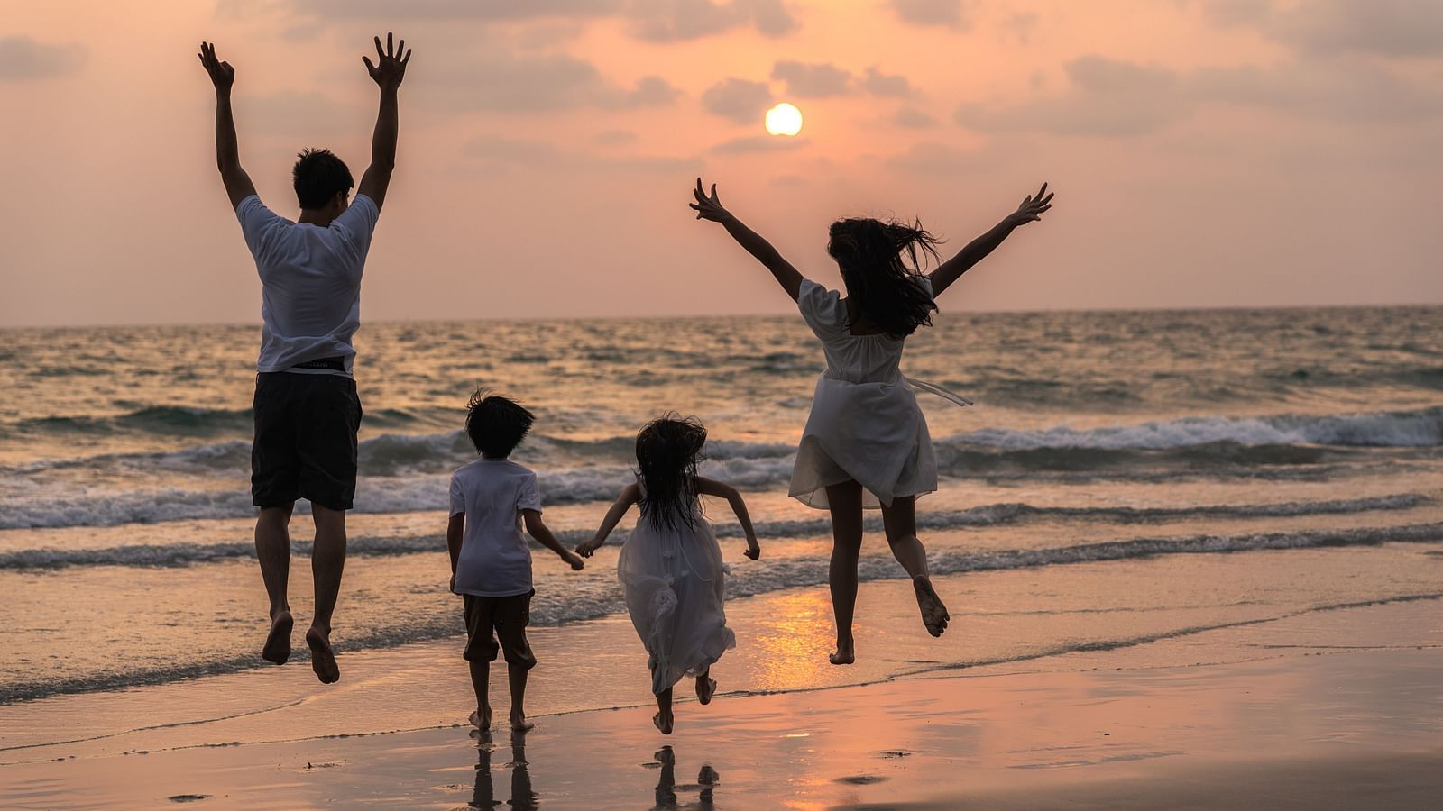 Family enjoying a beach vacation at sunset, with mom, dad, and child running and relaxing together near the sea.