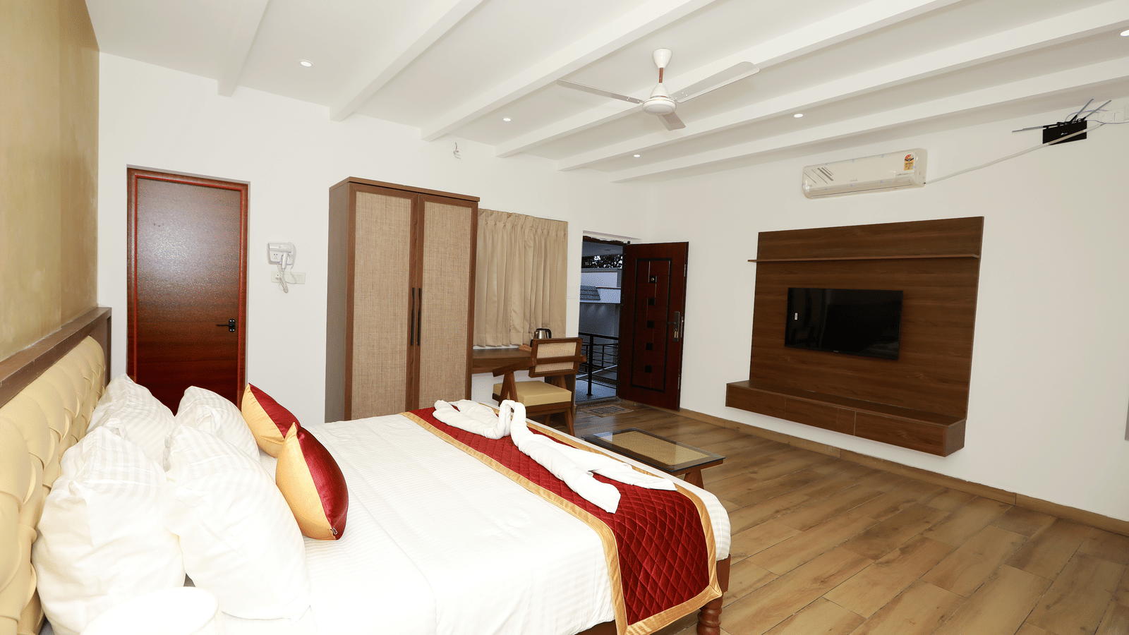 Corner view of the Nature Luxury Room featuring a double bed facing towards the wall-mounted television with the entrance door wide open in the corner at WOW Naturefull Resorts, Yercaud.