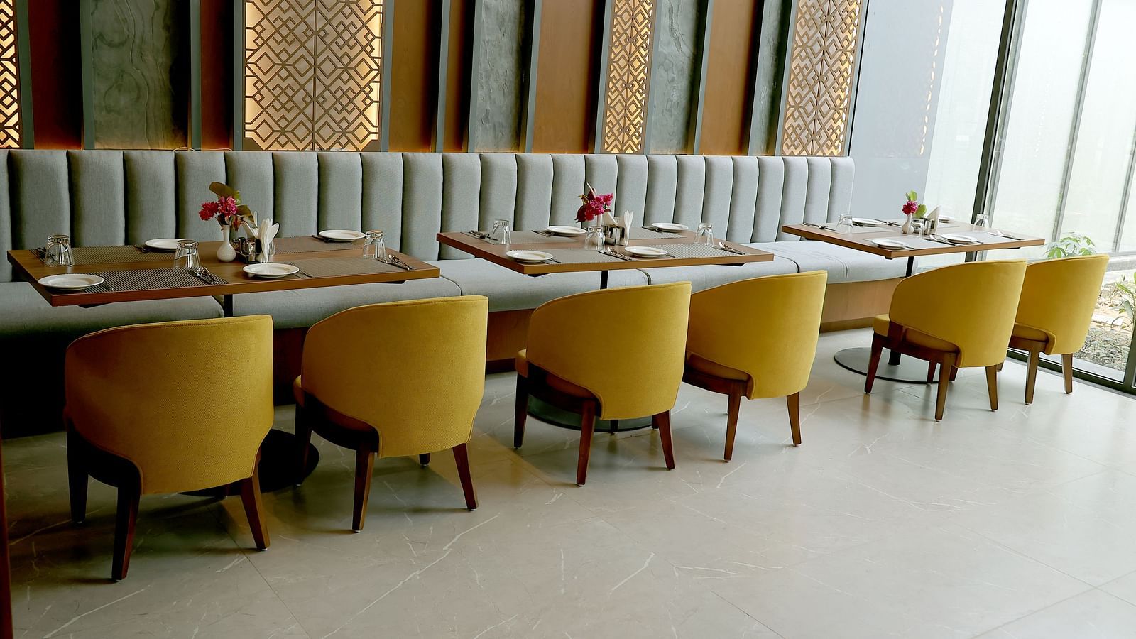 Elegant indoor dining area with mustard yellow chairs and a striped cushioned bench against a decorative wall at Wyndham Garden.