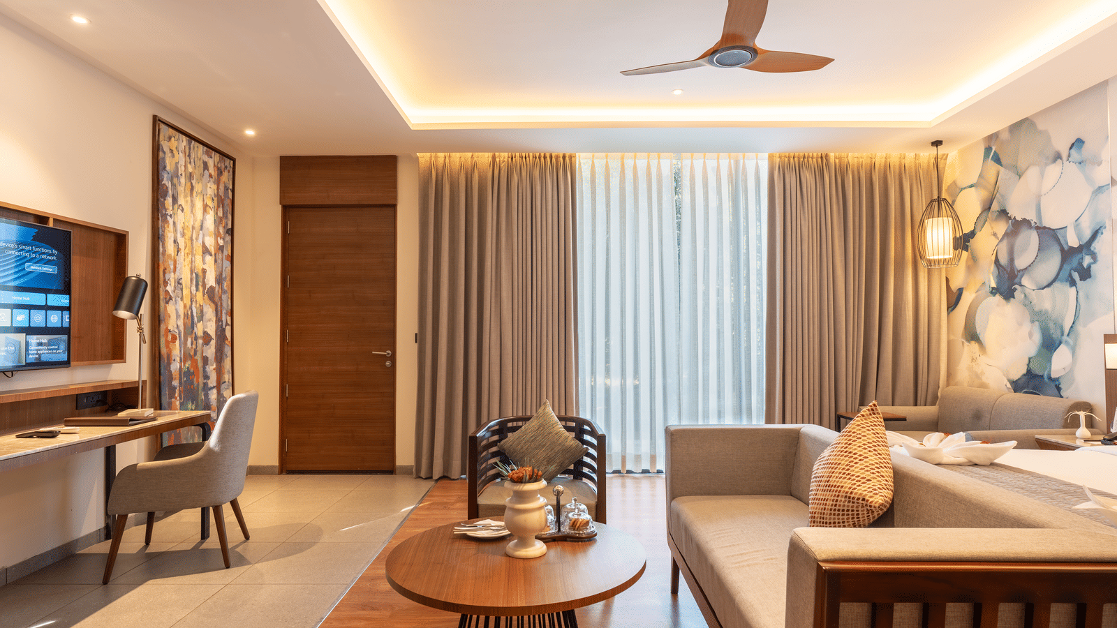 The living area of a guest room at Wyndham Garden with a  multi-seating sofa, a round table, a flat-screen television, and large glass windows