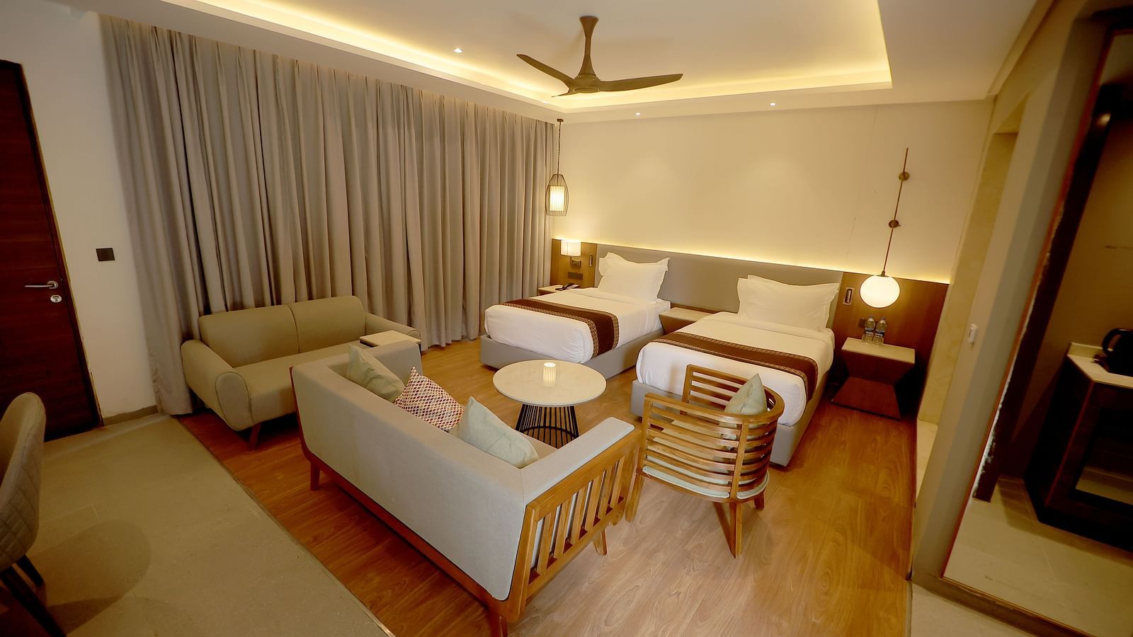 Spacious room with twin seating area, centre table, and ambient cove lighting above the bed at Wyndham Garden.
