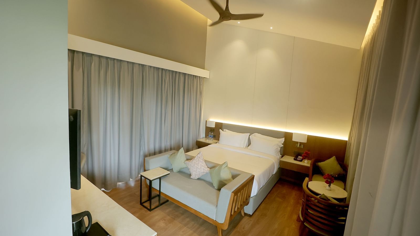 Bedroom with wooden flooring, soft lighting, and grey curtains, featuring a cushioned bench and ceiling fan at Wyndham Garden.