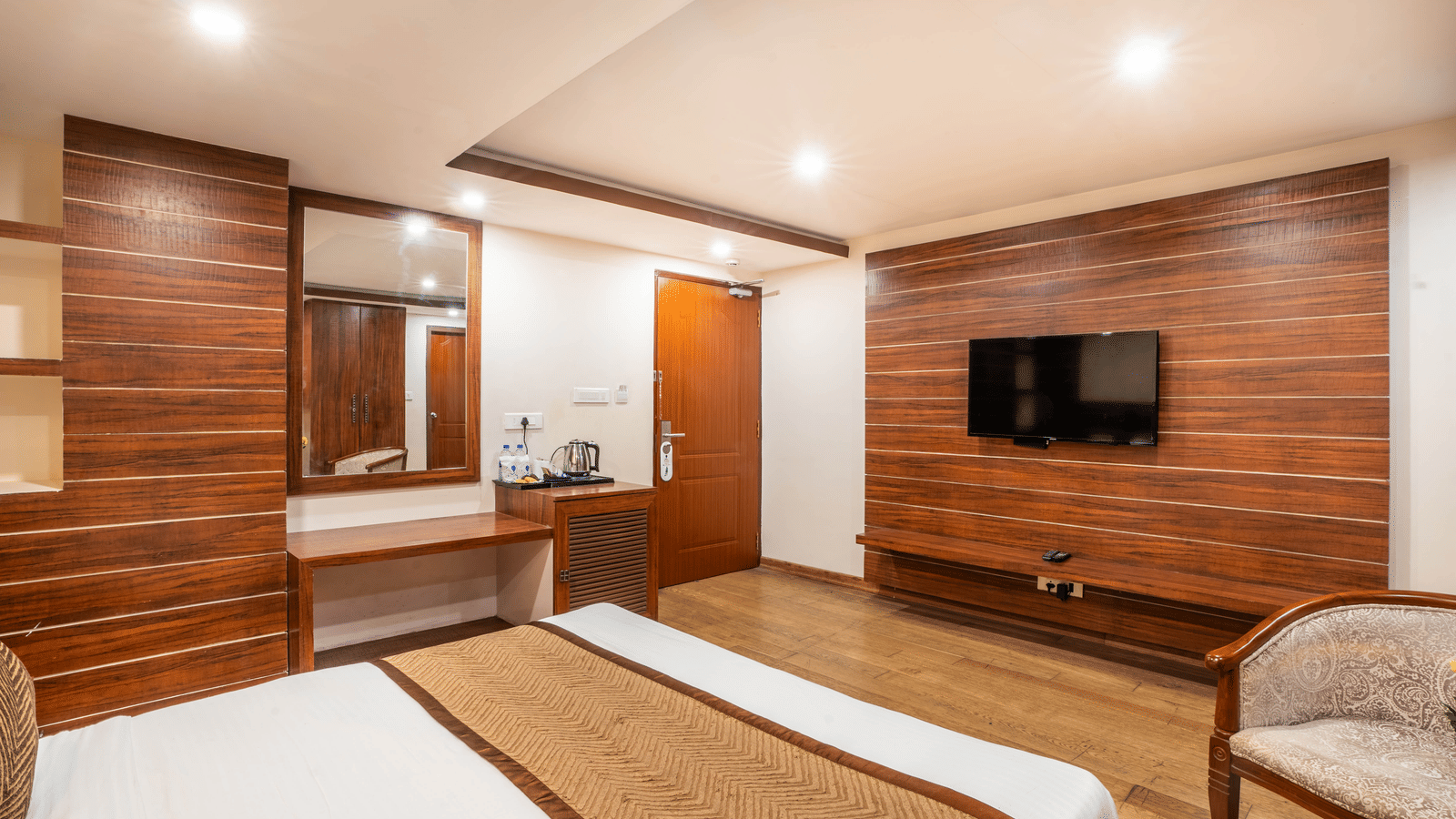 Bedroom with bed, chairs, and TV in wooden interior at Yashshree Jai Hotel & Banquet, Darjeeling.
