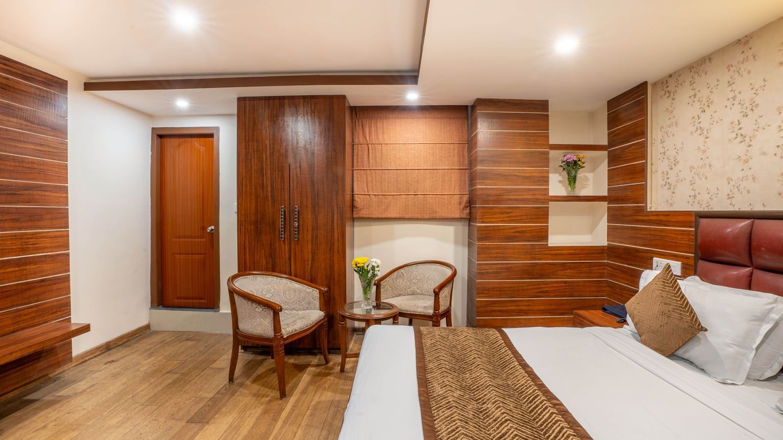 A cosy hotel bedroom with wooden flooring, a large bed, and a seating area at the Yashshree Jai Hotel & Banquet, Darjeeling.