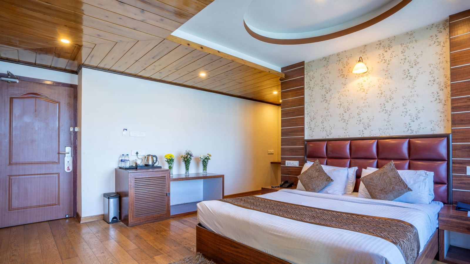 A stylish and well-lit hotel bedroom with a large bed, brown headboard, and wooden furnishings at the Yashshree Jai Hotel & Banquet, Darjeeling.