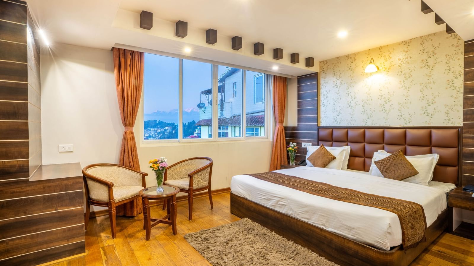 A well-appointed hotel room with a large bed, brown headboard, and seating area at the Yashshree Jai Hotel & Banquet, Darjeeling.