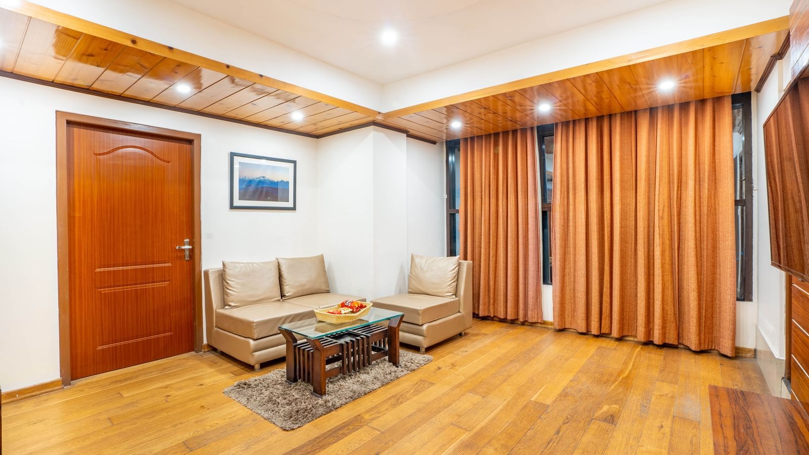 A hotel suite's living room with comfortable sofas, a wooden coffee table, and curtains at the Yashshree Jai Hotel & Banquet, Darjeeling.