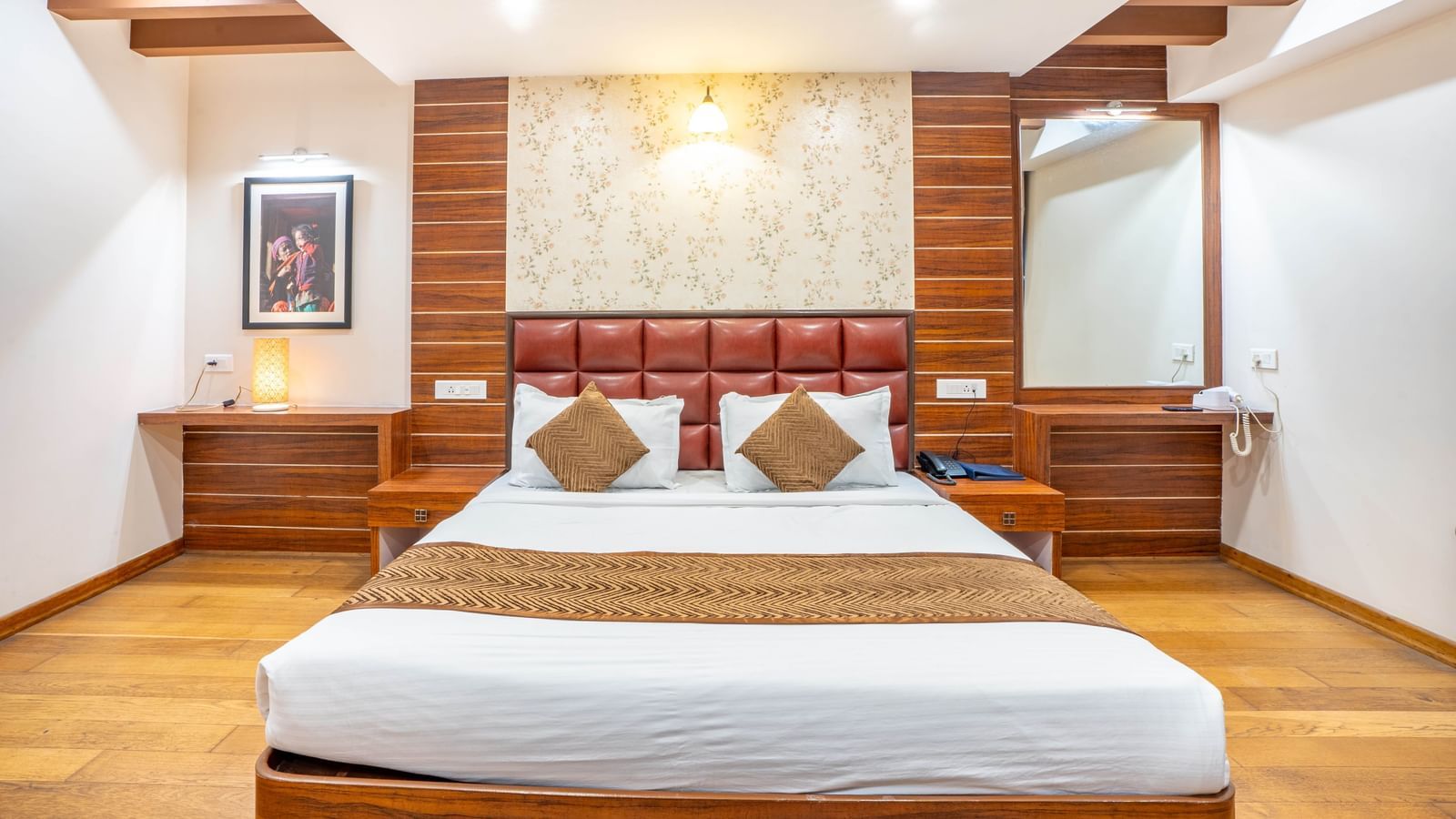 A modern and well-lit hotel room with a large bed, wooden furnishings, and a vanity at the Yashshree Jai Hotel & Banquet, Darjeeling.