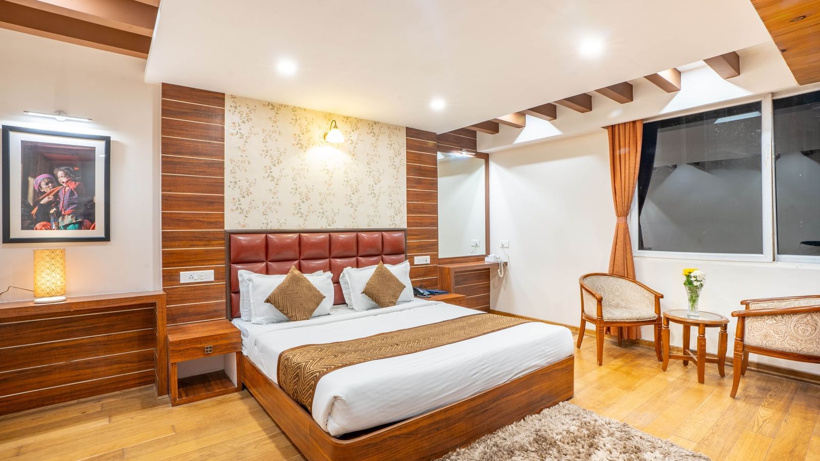 A comfortable hotel bedroom with a large bed, seating area, and a view of the street from the window at the Yashshree Jai Hotel & Banquet, Darjeeling.