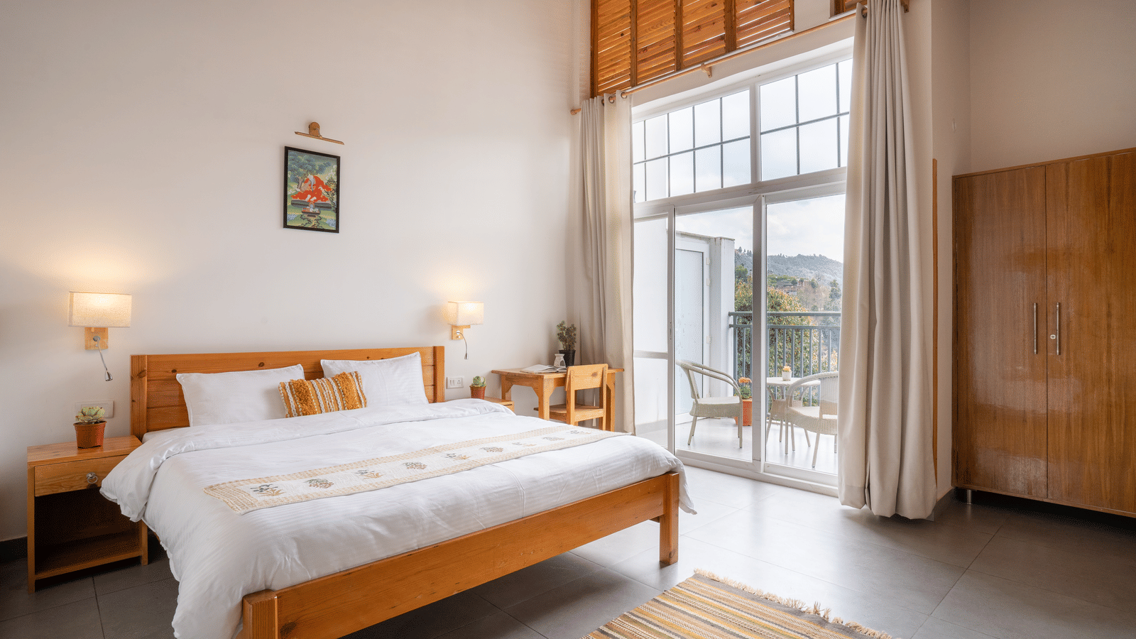 A wide shot of a Ziran Retreat bedroom with a large bed, wooden furniture, and a floor-to-ceiling window looking out at a scenic view.