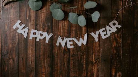 Happy New Year text banner with party hats and decorations hanging on rustic wooden background.