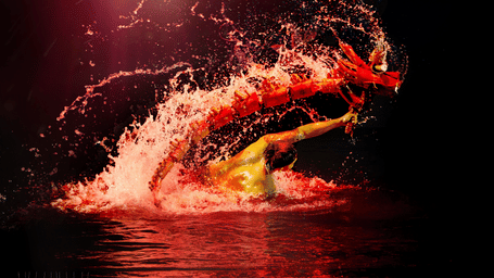 A performer in a dynamic pose amid bright red and orange water splashes.