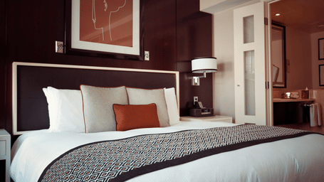 A luxurious hotel bedroom with a large bed, dark wood panelled walls, and an adjoining en-suite bathroom visible through glass doors.