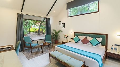 full view image of the king size bed and a seaing area with blue cushioned seats at the luxury pond view villas at aranya vilas