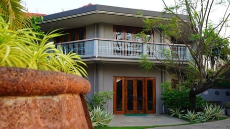 A facade of  Argo By Trance, Goa with a balcony and wooden doors, surrounded by lush tropical plants and trees
