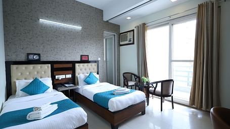 A hotel room featuring two beds, a seating area, and curtains - Asian Suites Cyber Park, Gurgaon.