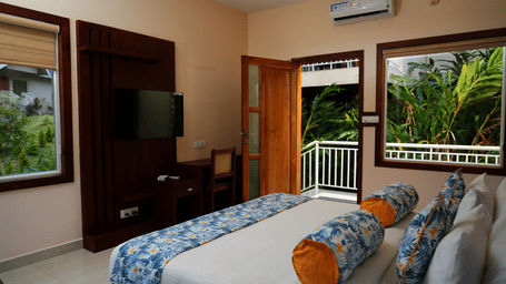 An overhead shot of the Luxe Mountain View Cottage featuring a double bed and a door opening to a balcony with lush green views at Aveda Mountains and Mist Resort and Spa, Munnar.