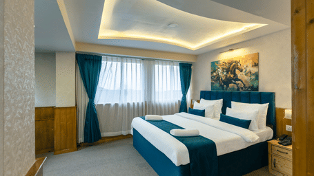 Deluxe Room with a king size bed, inviting ambiance, wooden bedside table, and a large window with curtains drawn at Avianna Seven Seas, Darjeeling.