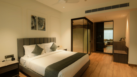 A king size bed, a wardrobe with a full length mirror, and a glass partition at Awesome Palace, Guwahati Airport.