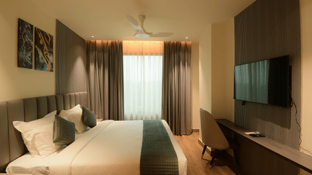 A king size bed facing a wall mounted television, a desk, and curtains at Awesome Palace, Guwahati Airport.
