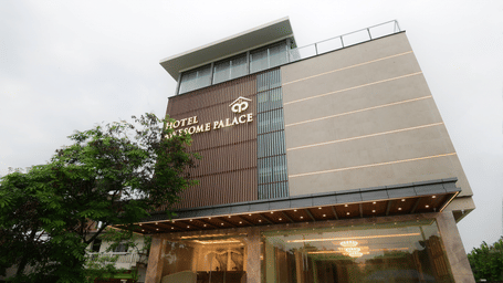 A multi-storey modern building with glass panels, signage on the facade, and large ground floor windows at Awesome Palace, Guwahati Airport.