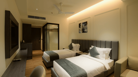 A room featuring twin beds, a wall mounted television, and a sofa chair at Awesome Palace, Guwahati Airport.