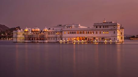 Palace lit at dusk, reflecting in water, with a soft sky.