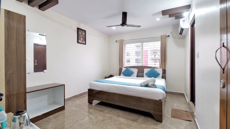 Clean contemporary guest room showing a double bed, ceiling fan, and built-in wardrobe with a mirrored vanity unit at beestay Hotels, MVP Colony, Vizag.