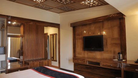 A cosy hotel room featuring a large bed, wooden furnishings, and a wall-mounted television at Benzz Park, Kodaikanal.