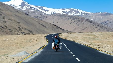 A traveller riding a bike on a remote highway surrounded by mountains