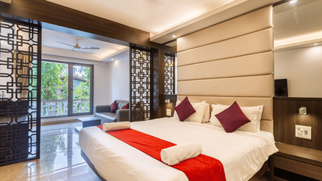 Room with a plush bed, red accents, and a cozy seating area at CALUX Joia Do Mar Resort, Goa, filled with warm natural light