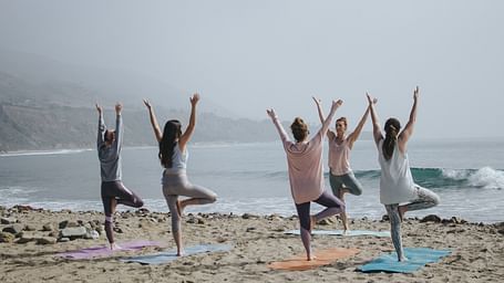 A group of people performing yoga on the beach while looking in to the horizon.