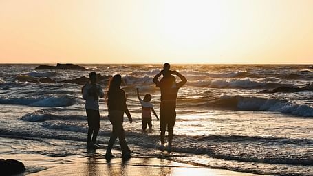A family of five playing on a beach with the sun setting in the background.