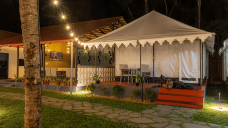 Exterior of a lit luxury tent at night with string lights and a stone garden path.